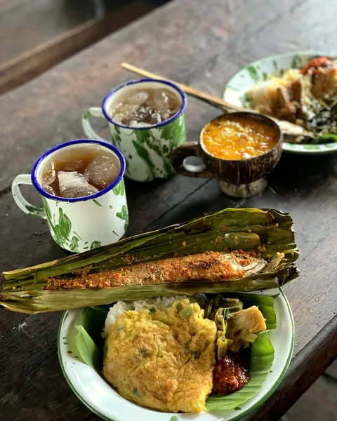 Gelas blirik berisi teh dan lauk berbungkus daun pisang di meja kayu (foto ilustrasi)